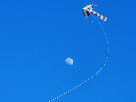 rainbow colored kite with its string going around a partial moon visible in the background