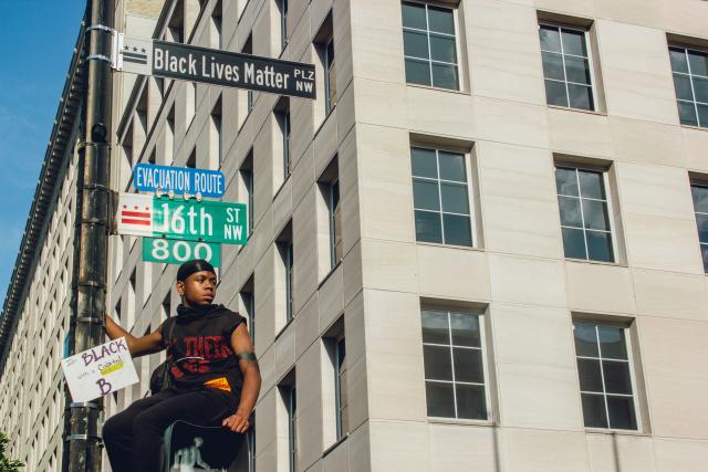 Boy sitting on a crossing light box on a road sign in Washington, D.C.